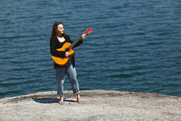 girl with a guitar in her hands on the shore, in the background the blue sea