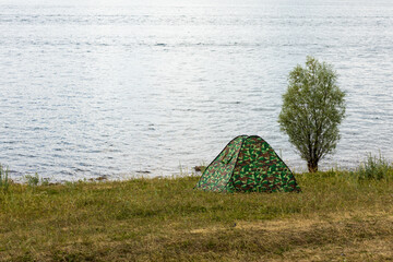 camouflage tent and a lonely tree on the shore