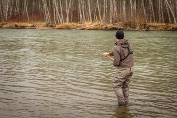 A fly fisherman hooked into a big fish in a river with the rod bent