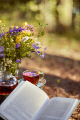 Tea party in the open air. Close-up of a Cup and teapot in nature in the forest. A bouquet of flowers and a book