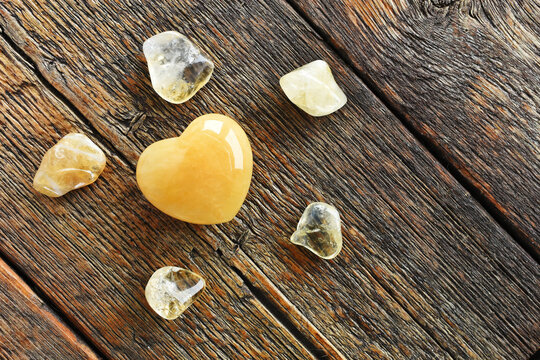 A top view image of a yellow calcite heart shaped crystal on a dark wooden table top. 