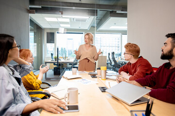 Obraz premium Mature woman standing by table in front of her young intercultural colleagues