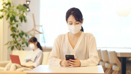 マスクをしてスマホを見る女性 © metamorworks