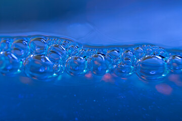 Blurred background with water line and bubbles in blue tones in high magnification.