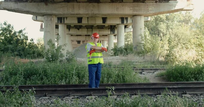 Confident senior railroader stands on railway and crossing hands at camera