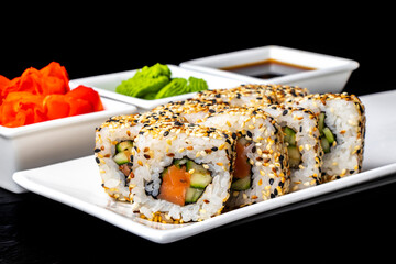 Rolls with salmon, cucumber and sesame seeds on a white plate on a dark background. Sushi menu. Japanese food.