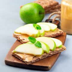 Healthy sandwich with low carb whole grain cracker, green apple slices and peanut butter, on  wooden board, square format