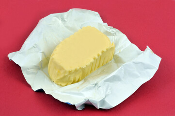 Plaquette de beurre dans son emballage ouvert sur fond rouge