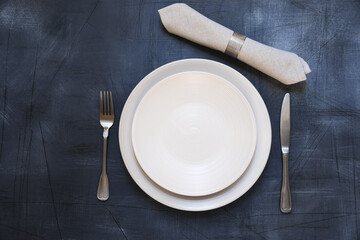 Table setting. White craft plate, cutlery and napkin on dark stone table. Top view, copy space, Table setting. background for menu, layout, place for text 