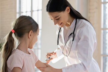 Smiling female pediatrician wearing uniform with stethoscope vaccinating little girl in hospital, doctor gp making prick, injection to preschool girl in clinic, children healthcare concept