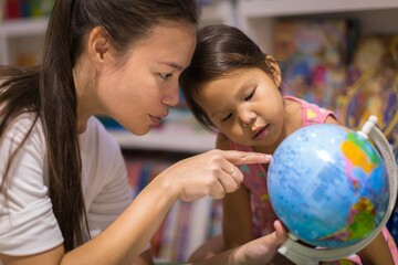Parent showing a world globe to her kid. Children learning geography.