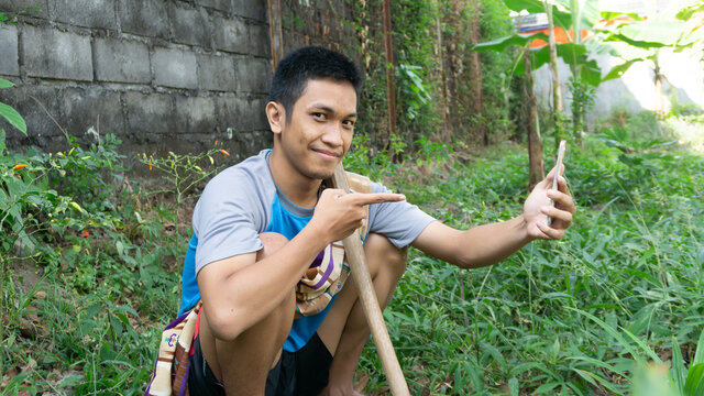 Asian man is gardening and thinking while looking at his cellphone