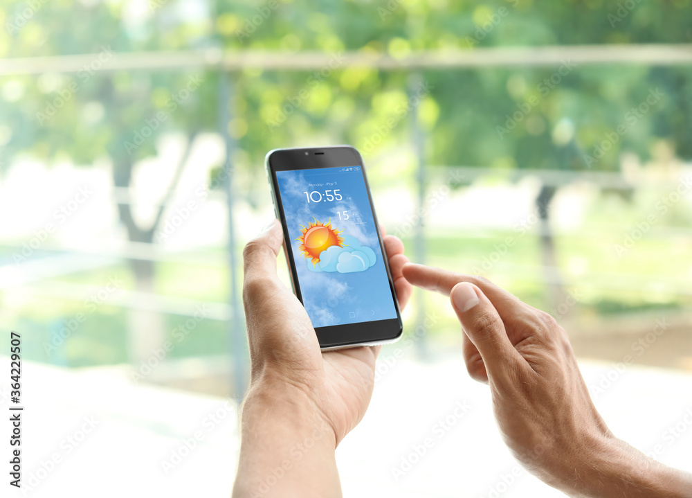 Wall mural man using weather forecast app on smartphone near window, closeup