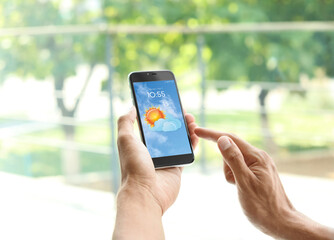 Man using weather forecast app on smartphone near window, closeup