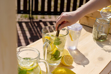 Hand of young woman squeezing lemon slices in glass jug with water outdoors