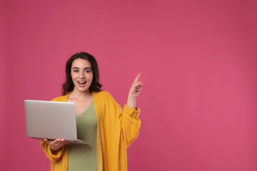 Young woman with laptop on pink background. Space for text