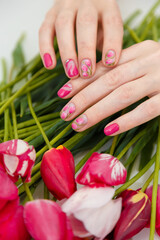 Obraz na płótnie Canvas Female hands with spring manicure and tulips nail art, floral design on flowers background. Beauty, fingernails and hands care concept. Vertical shot.