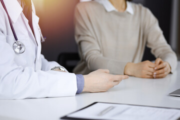 Unknown male doctor and patient woman discussing something while sittingin a darkened clinic, glare of light on the background. Close-up of hands