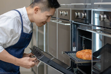 Asian baker smile and looking at the fresh baked bread from the oven in the kitchen. Man cooking ...