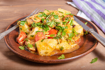 Italian cuisine - Arrabbiata garlic chicken with potatoes in a clay plate on the table, close-up, rustic style