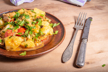 Italian cuisine - Arrabbiata garlic chicken with potatoes in a clay plate on the table, close-up, rustic style