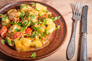 Italian cuisine - Arrabbiata garlic chicken with potatoes in a clay plate on the table, close-up, top view, rustic style