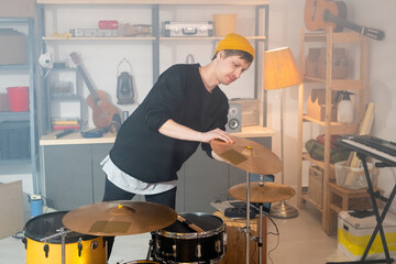 Contemporary young musician bending over drum kit while checking cymbals