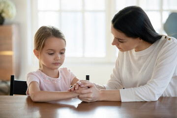 Caring mother holding upset offended little daughter hands close up, sitting at desk, expressing...