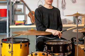 Young musician in casualwear beating one of drums with wooden drumsticks