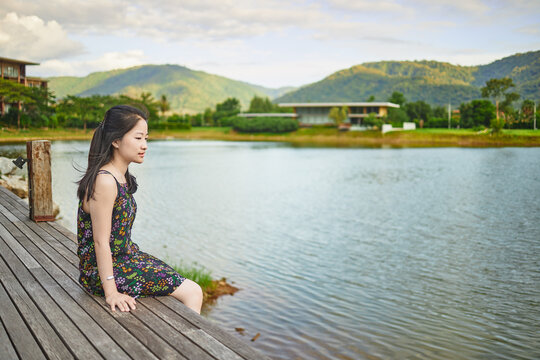 Asian girl sitting on wooden bridge in garden at evening