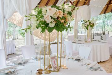 Beautiful floral arrangement of rose flowers and greenery in tall vase on wedding table in...