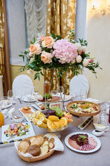 Beautiful floral arrangement of rose flowers and greenery in tall vase on wedding table in restaurant, copy space. Luxury wedding decorations. Table setting