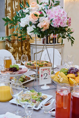 Beautiful floral arrangement of rose flowers and greenery in tall vase on wedding table in restaurant, copy space. Luxury wedding decorations. Table setting