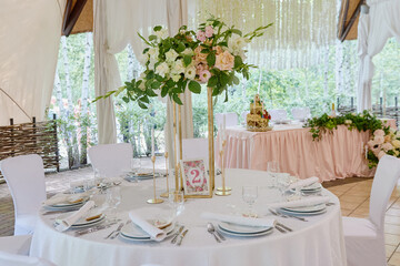 Table setting with lush bouquet on table, copy space. Place setting at luxury wedding reception. Round table and white chairs served for wedding banquet in restaurant