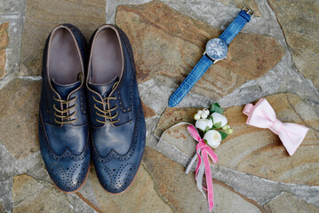 Blue leather male shoes, watches, boutonniere and pink bowtie on brown stone background, copy space. Groom wedding accessories. Top view, flat lay