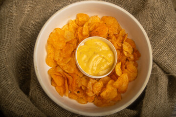 Potato chips on a round platter and a saucepan with cheese sauce. Close up.
