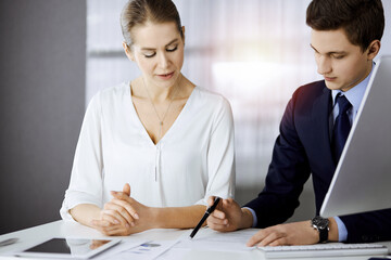 Fototapeta premium Business people discussing something while sitting in sunny office. Focus at businesswoman while talking to her male colleague