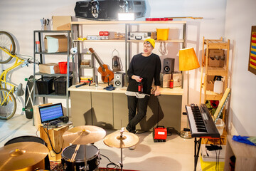 Young restful musician in casualwear having bottle of beer at break in garage