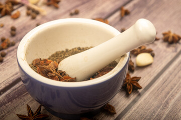 Allspice in a ceramic mortar and scattered garlic cloves, star anise and allspice on a wooden table. Close up.