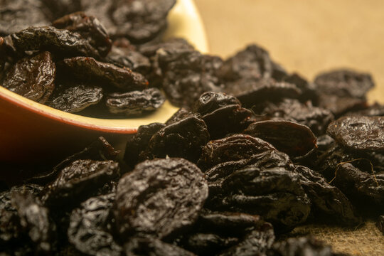 Dried prunes in a ceramic bowl and dried prunes scattered on a background of coarse-textured burlap. Close up.