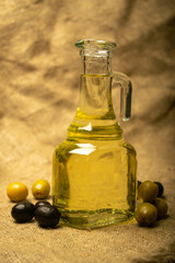 A glass bottle of olive oil on a background of green olives, black olives and homespun fabric with a rough texture. Close up.