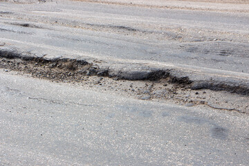 Poor condition of the road surface. Spring season. Hole in the asphalt, risk of movement by car, bad asphalt, dangerous road, potholes in asphalt. Moat on the asphalt