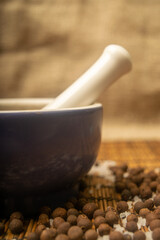 Ground black allspice in a ceramic mortar and black allspice and coarse salt scattered on a reed Mat. Close up.