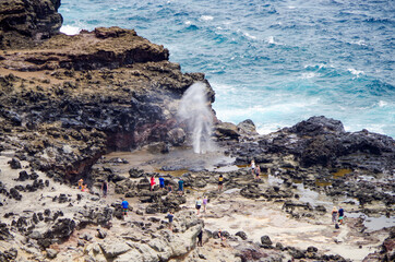People standing around Nakalele Blowhole Geysir at rocky coast line or shore on North Maui Island...