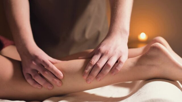 Close-up of the hand massage of the calf muscle. A professional massage therapist massages a woman's leg in an office with a beautiful light