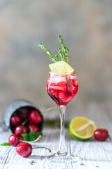 Cherry red cocktail with lime. Fresh summer cocktail with cherries, thyme and ice cubes.