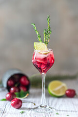 Cherry red cocktail with lime. Fresh summer cocktail with cherries, thyme and ice cubes.