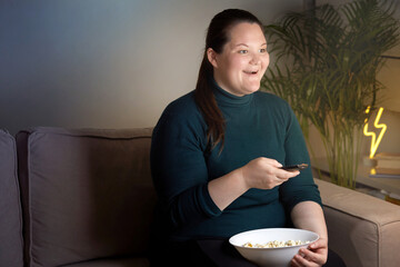 The girl smiles and holds in her hand a remote control for controlling the TV.