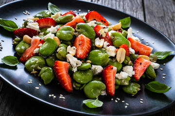 Broad beans salad with feta cheese and strawberries on wooden table
