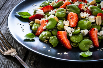 Broad beans salad with feta cheese and strawberries on wooden table
